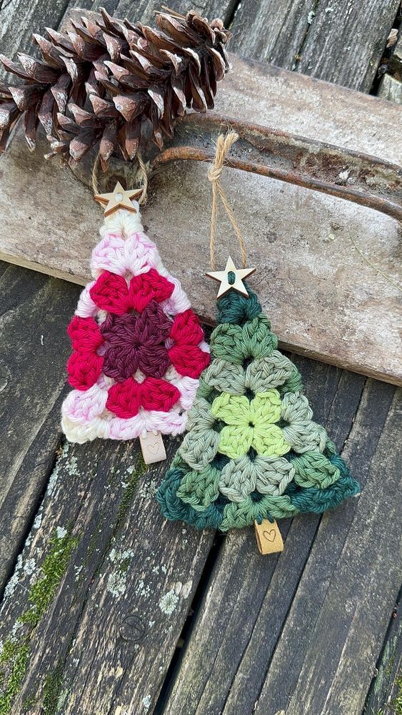 two crocheted christmas tree ornaments sitting on top of a wooden table next to a pine cone