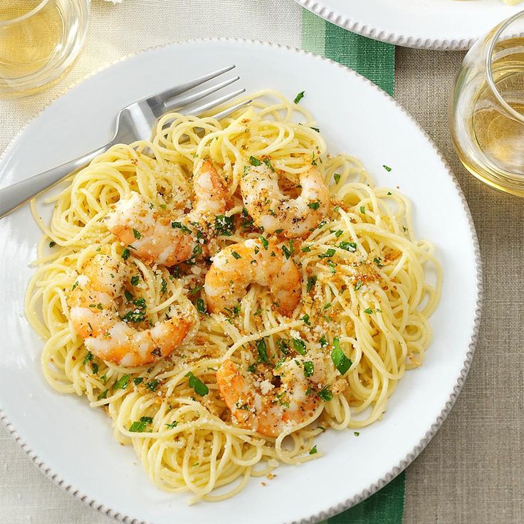 a plate of pasta with shrimp and parmesan cheese on the side next to two glasses of wine