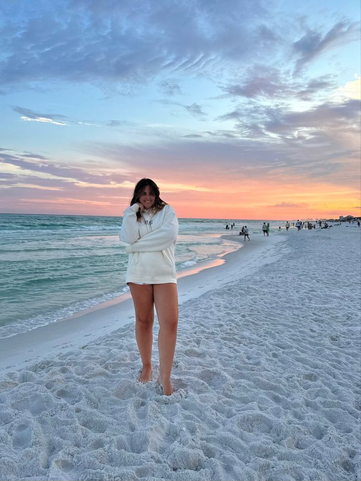 a woman standing on top of a sandy beach next to the ocean at sunset or dawn