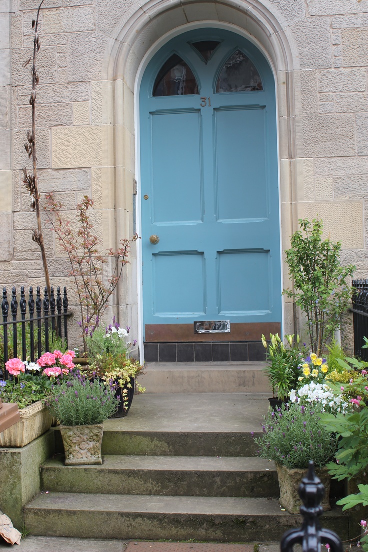 a blue door is on the side of a building with potted plants and flowers