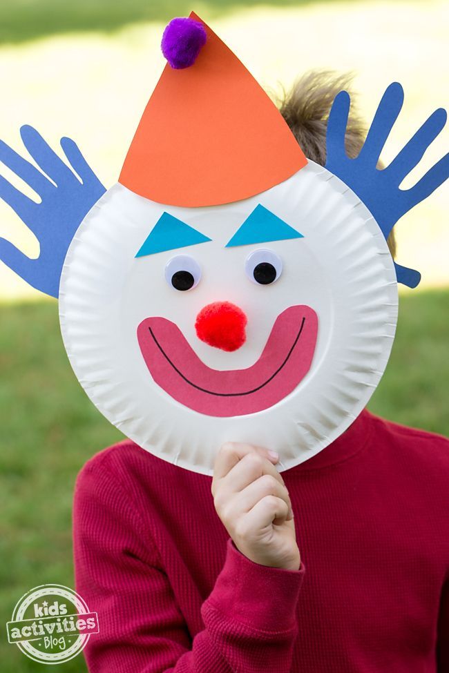 a child holding up a paper plate with a clown mask on it's face