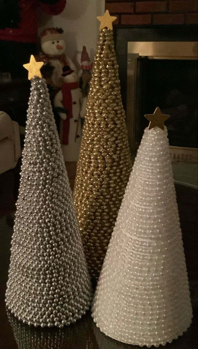 two christmas trees made out of plastic beads on a table in front of a fireplace