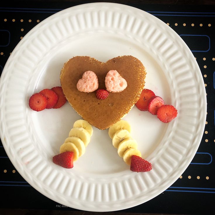 a heart shaped dessert on a paper plate with strawberries and banana slices around it