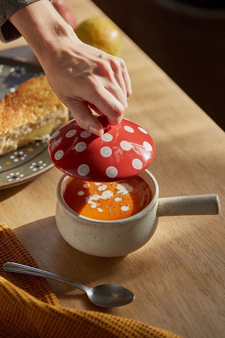 a person dipping sauce into a bowl on a wooden table next to bread and an apple