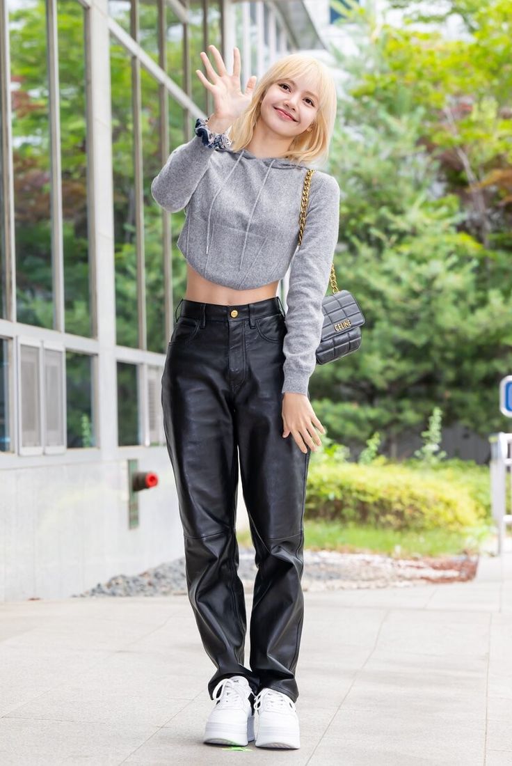 a woman in black leather pants and grey sweater waving