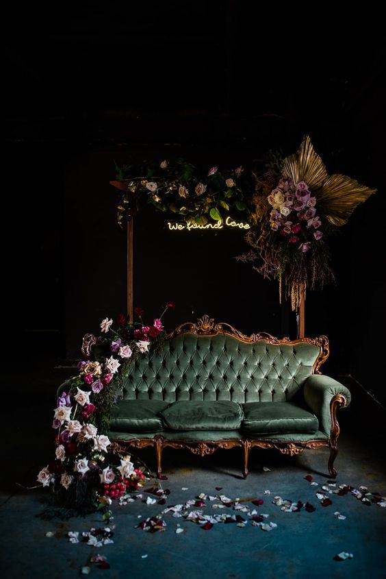 a green couch sitting in front of a flower covered table with flowers on it and petals all over the floor