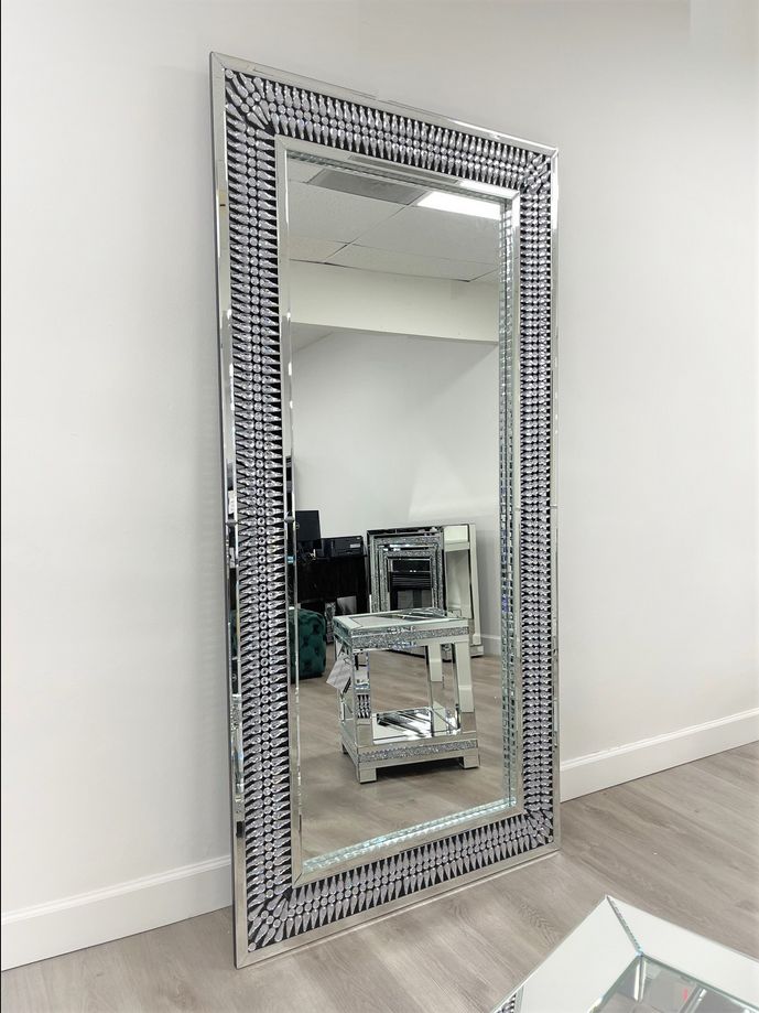 a mirror sitting on top of a wooden floor next to a table with a vase