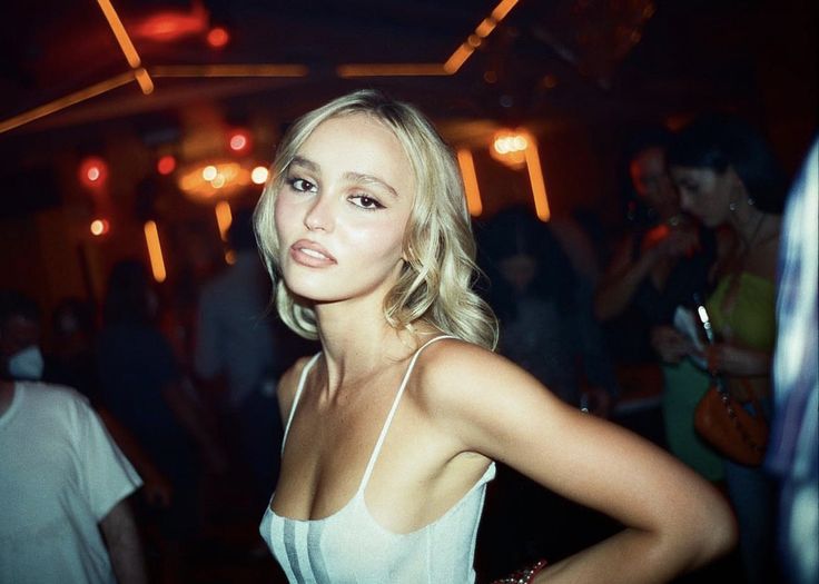 a woman standing in front of a group of people at a club or bar wearing a white tank top