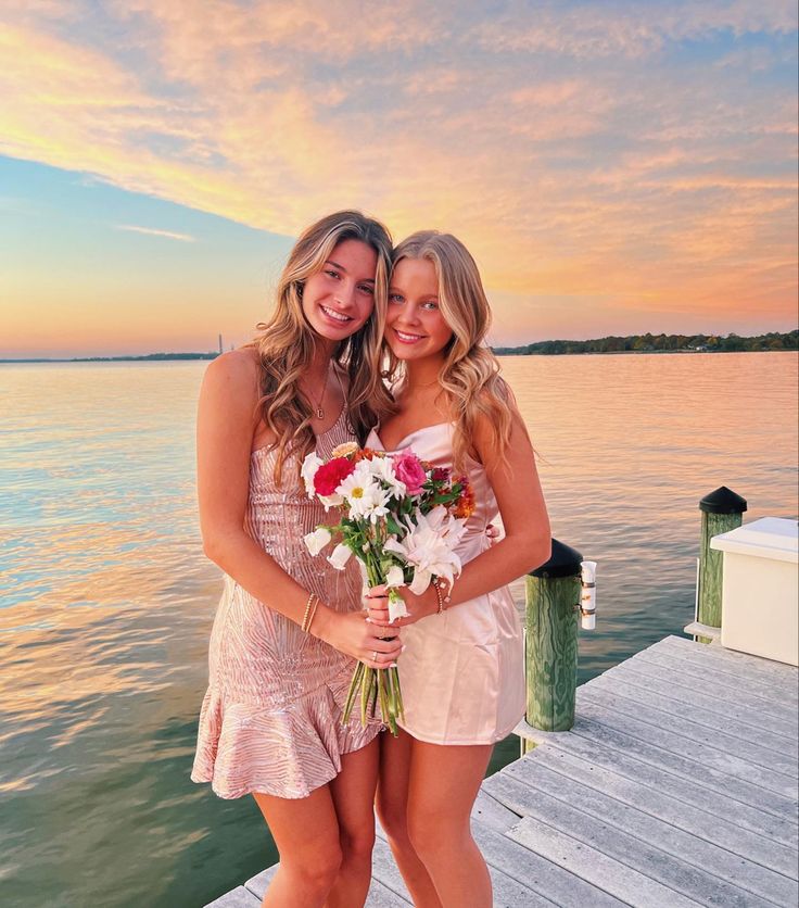 two beautiful young women standing next to each other on a pier