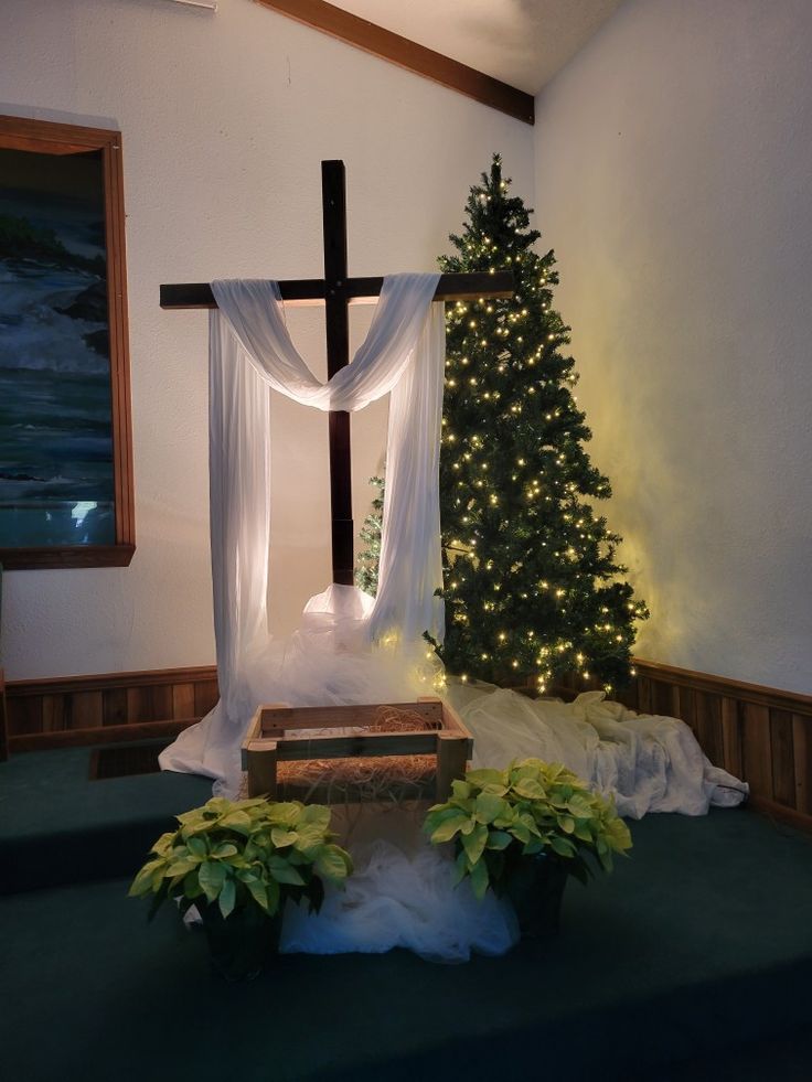 a christmas tree in the corner of a room with a cross on it and lights hanging from the ceiling