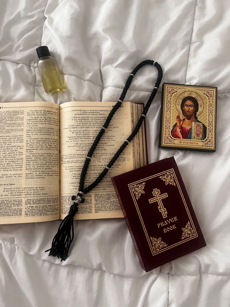 an open book with a cross and rosary on it next to a bottle of oil