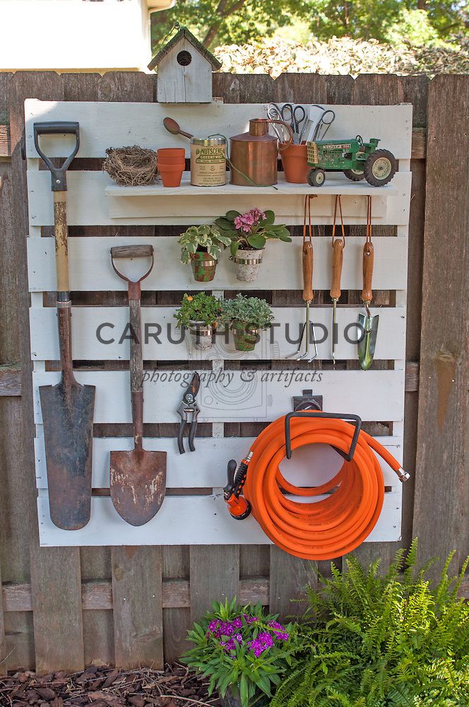 garden tools are hanging on a wooden fence