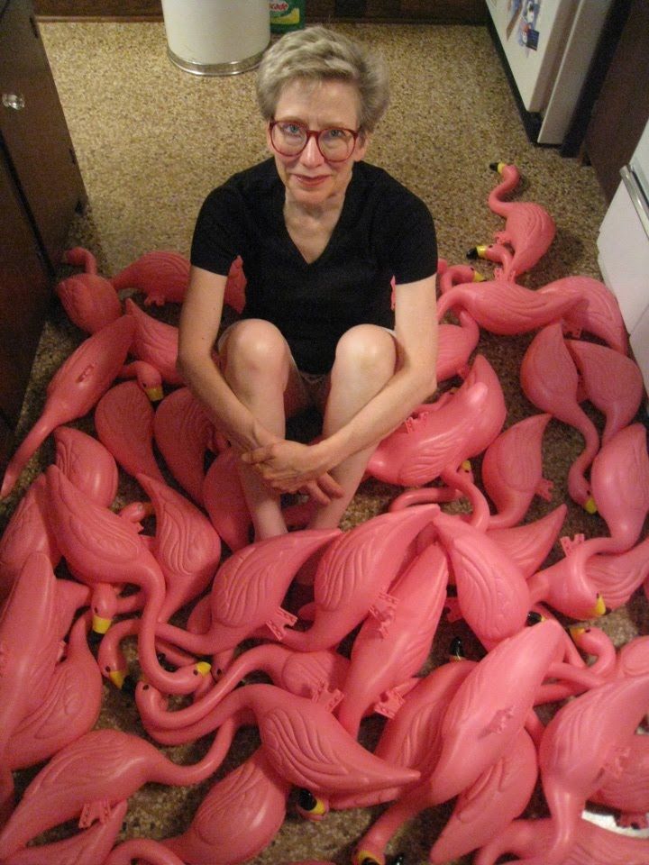 a woman sitting on the floor surrounded by pink plastic flamingo sculptures in a kitchen