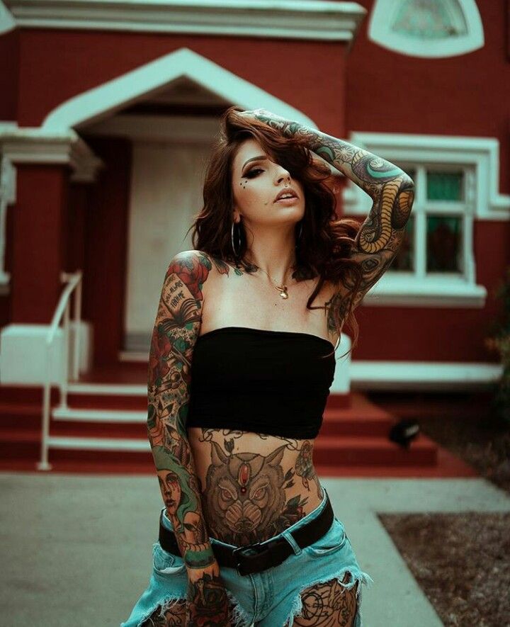 a woman with tattoos standing in front of a house