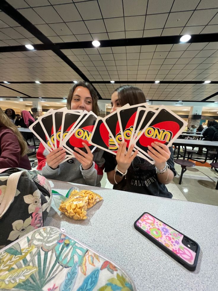 two women holding up cards in front of them at a table with food on it