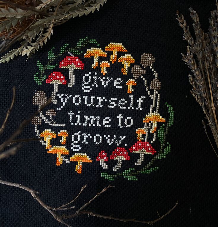 a cross stitch design on a black background with some dried grass and branches in the foreground