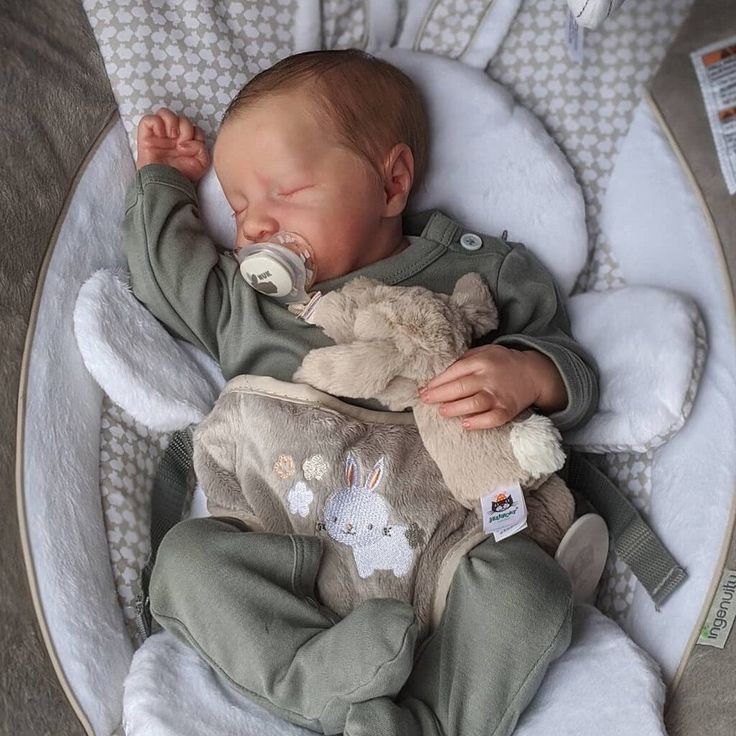 a baby sleeping in a swing with a stuffed animal on it's back and eyes closed