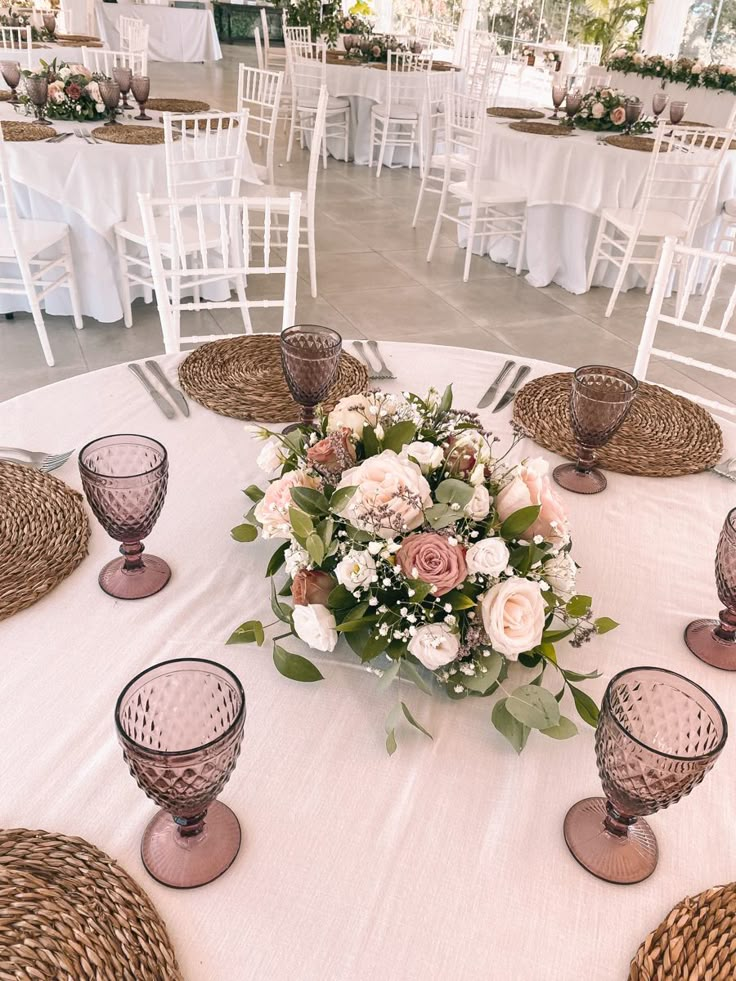 an arrangement of flowers on a table at a wedding reception with white linens and wicker place settings