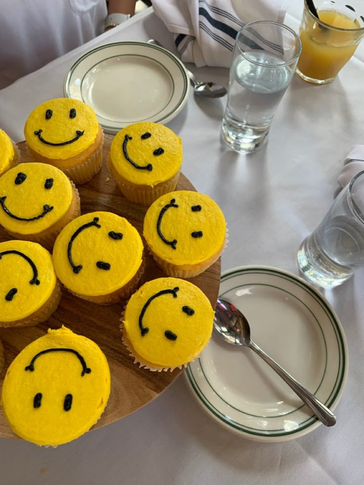 cupcakes with yellow frosting and smiley faces on them sitting on a wooden platter