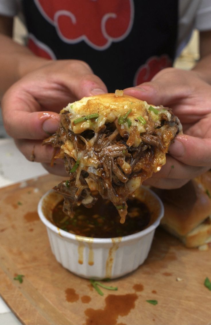 a person is holding up some food in front of their face and dipping it into a small bowl