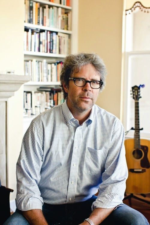 a man with glasses sitting in front of a book shelf