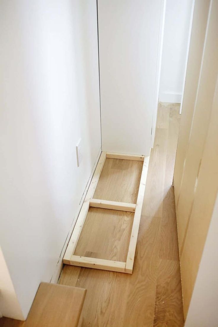 a wooden step leading up to a white wall in a room with hardwood flooring