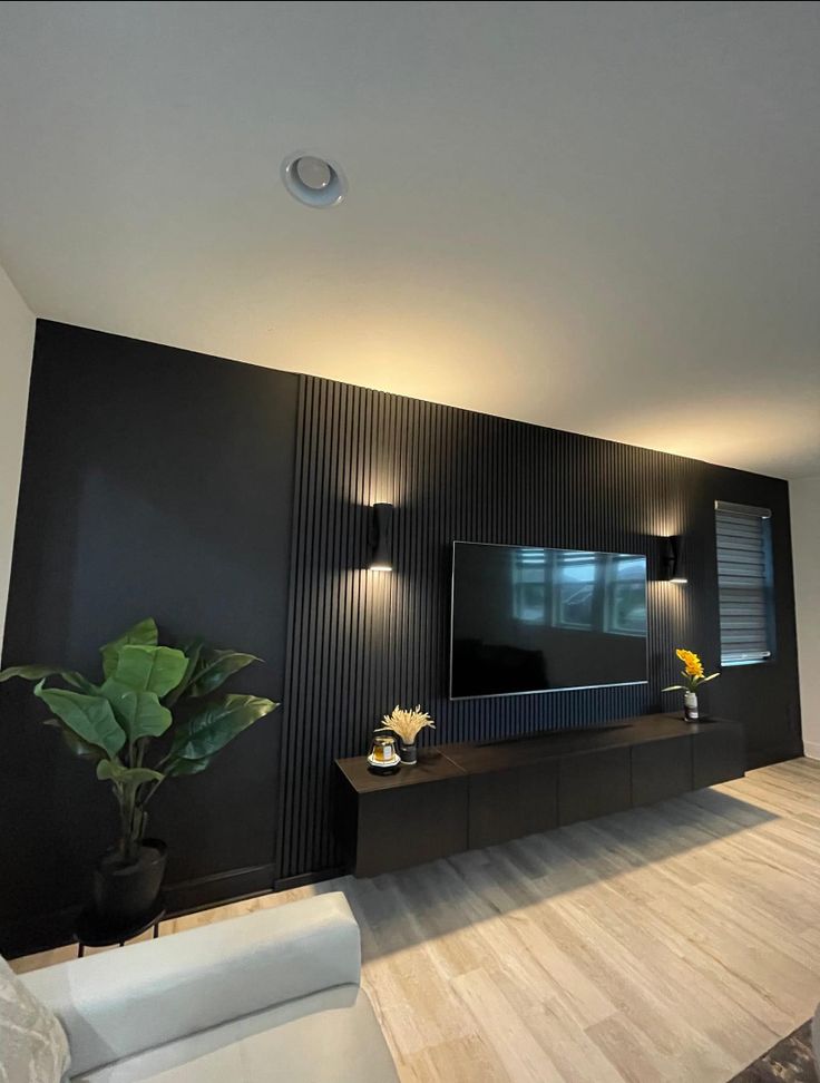 a modern living room with black walls and white couches in front of a flat screen tv