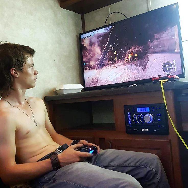 a shirtless man sitting in front of a tv holding a game controller and looking at the television