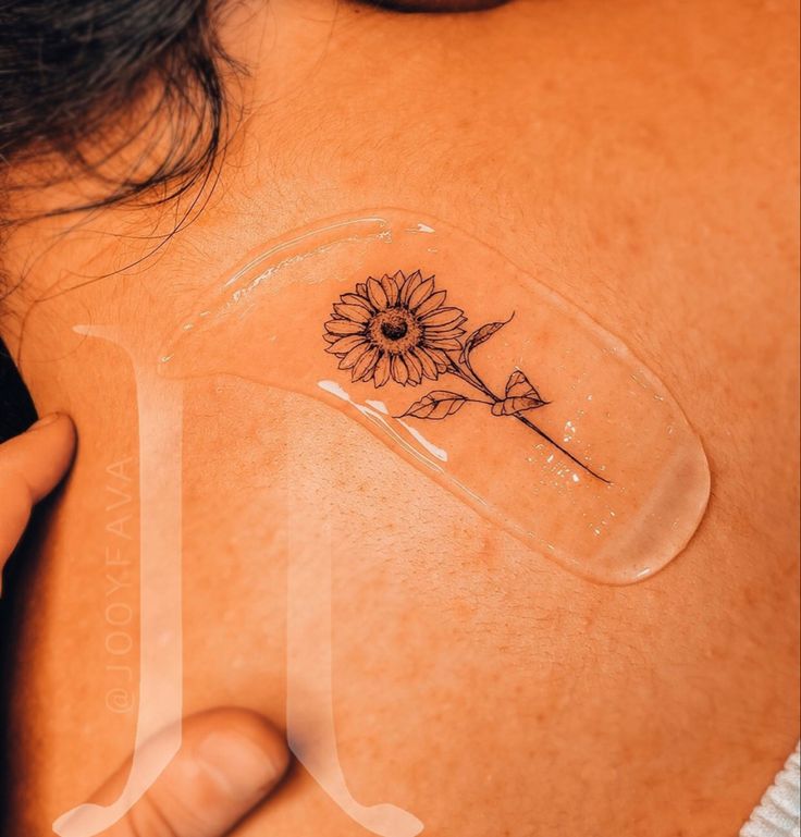 a woman with a sunflower tattoo on her upper back shoulder and arm, holding onto a piece of clear acrylic