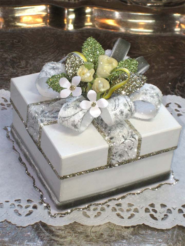 a white gift box with flowers and ribbons on it sitting on a lace doily