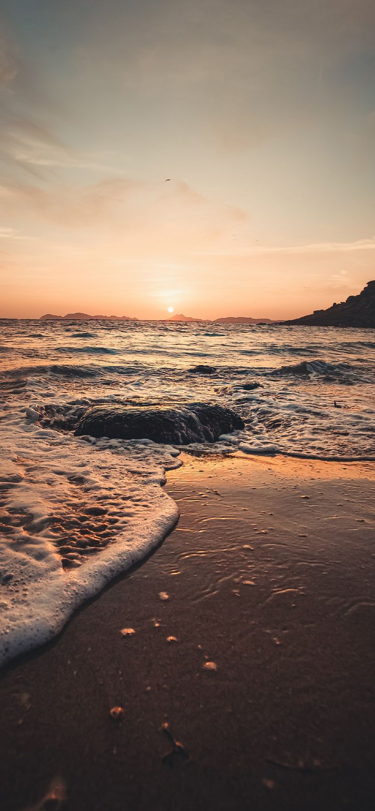 the sun is setting over the ocean with waves coming in to shore and an island in the distance