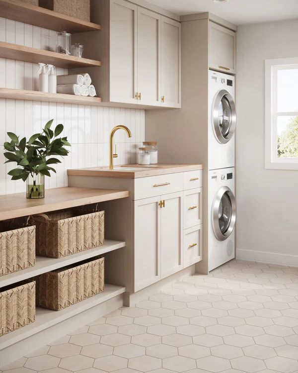 a washer and dryer in a kitchen with white cabinets, beige flooring and wooden shelves