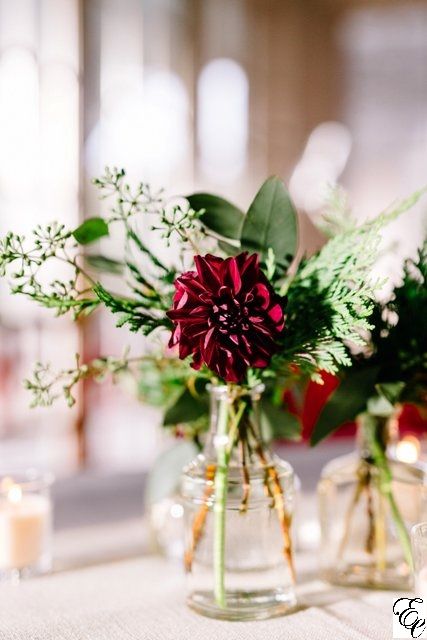 two vases filled with flowers and greenery on a white tablecloth covered table