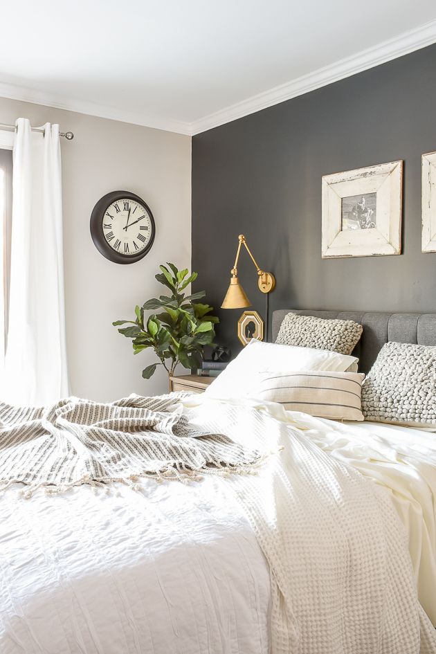 a bed with white sheets and pillows in a bedroom next to a window, clock on the wall