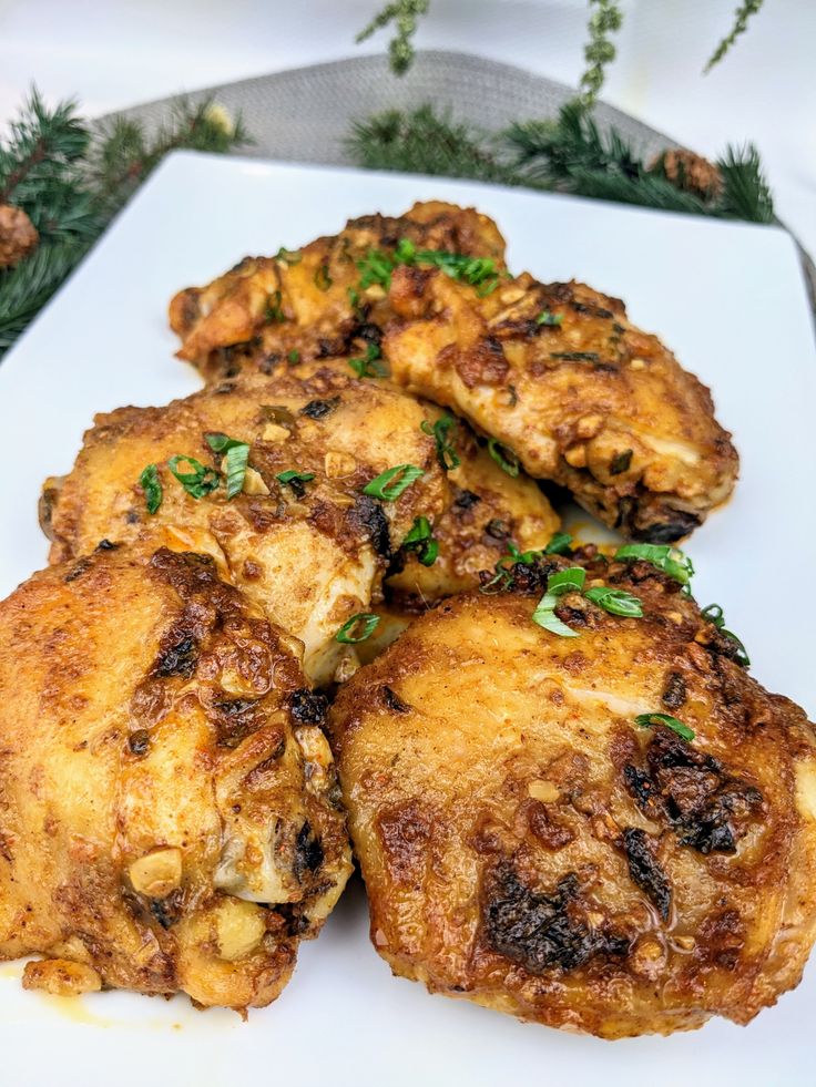 several pieces of fried chicken on a white plate with pine branches in the back ground