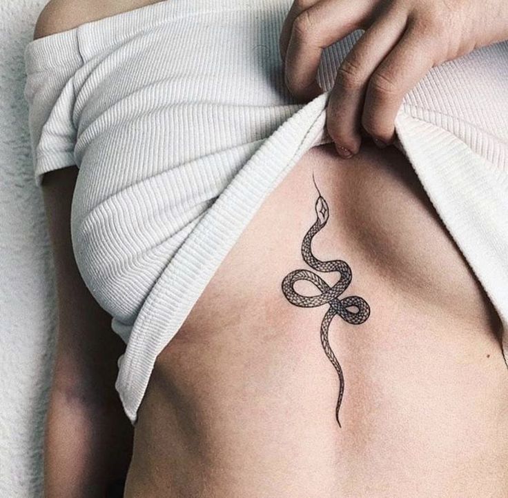 a woman with a snake tattoo on her side ribcage is shown from the waist up