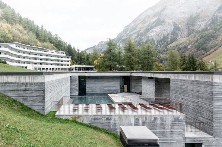 an outdoor swimming pool in the middle of a grassy area next to a building and mountains