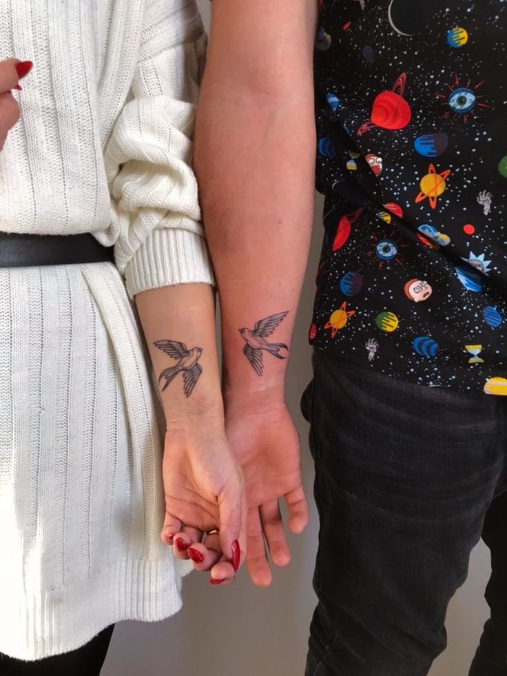 two people holding hands with small tattoos on their arms and one is holding the other's hand