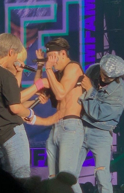 three shirtless men on stage with microphones in their hands and one man holding his mouth open