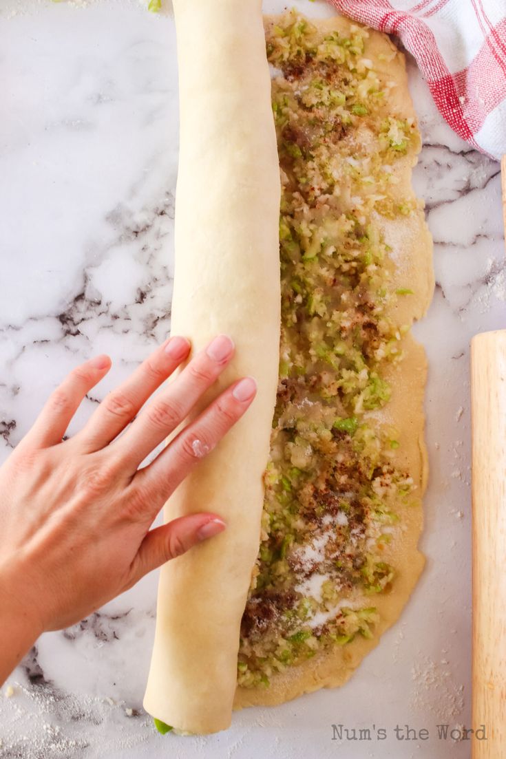 a person holding a long piece of bread on top of a marble counter next to a rolling pin