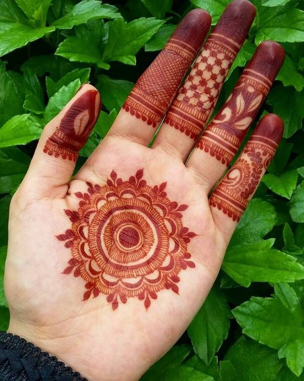 a hand with henna on it and some green leaves in the backgroud