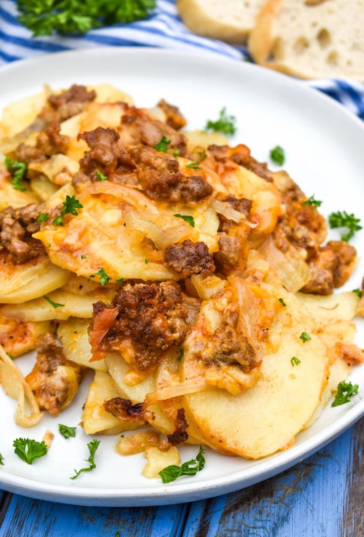 a white plate topped with ravioli and meat covered in sauce next to slices of bread