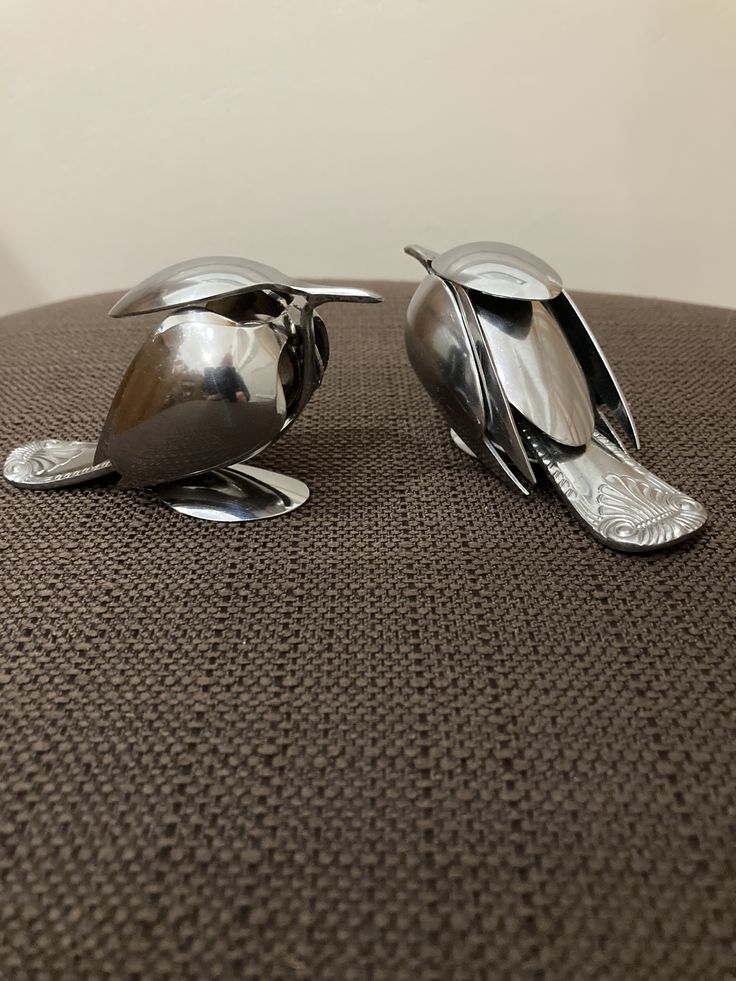 two metal spoons sitting next to each other on top of a brown tablecloth