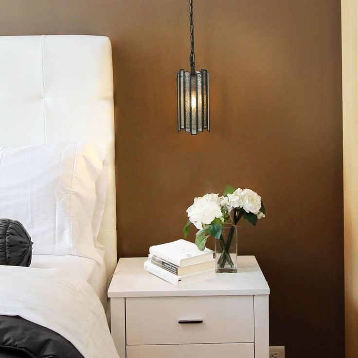 a nightstand with flowers and books on it next to a white bed in a bedroom