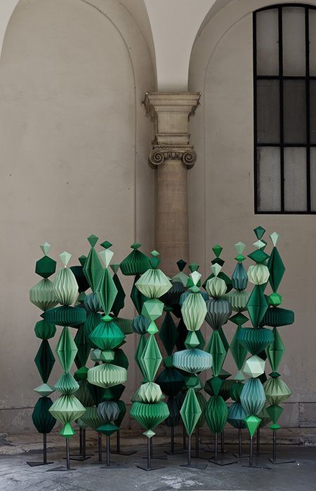 several green and white origami sculptures in front of a building with arched windows