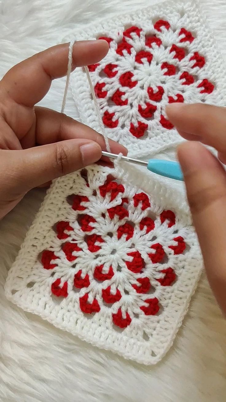 someone is crocheting the red and white square on their hand while they are knitting