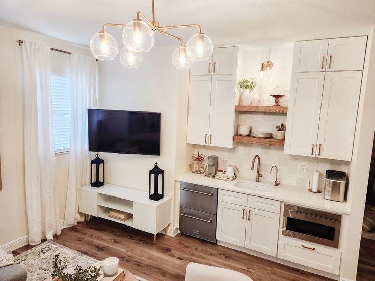 a living room and kitchen area with white cabinets, wood flooring and a flat screen tv mounted on the wall