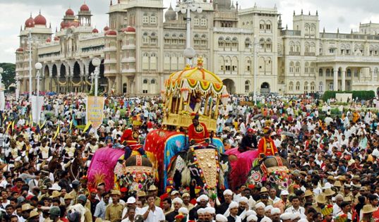 a large group of people standing in front of a building with an elephant on it's back