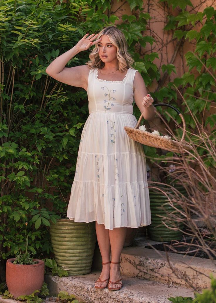 a woman in a white dress is holding a basket and posing for the camera with her hands on her head