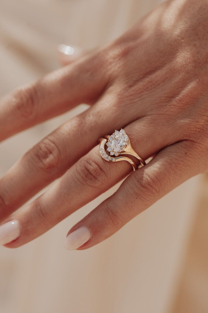 a woman's hand wearing a gold ring with a pear shaped diamond on it